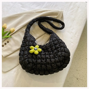 Detail view of black quilted bubble bag with a bright yellow flower charm on beige background