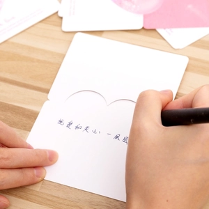 Close-up of a hand writing a message on a minimalist white 3D heart greeting card