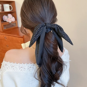 Detail of a black silk bow hair tie with white polka dots tied on a low ponytail