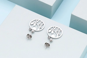 Macro shot of silver titanium stud earrings with hollow tree silhouette on blue blocks