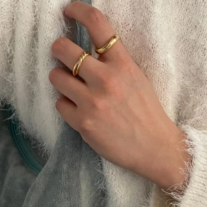 Gros plan de bagues dorées minimalistes lisses et torsadées sur un tissu blanc doux