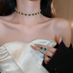 Detail of luxury gold necklace and earrings set with green gems and zircon on a model