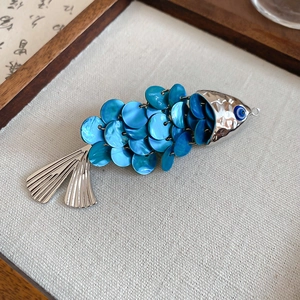 Macro detail of fish-shaped clip with blue iridescent shell scales and evil eye charm