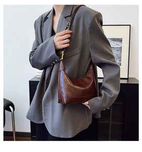 Close-up of brown leather shoulder bag with embossed texture and gold hardware on model