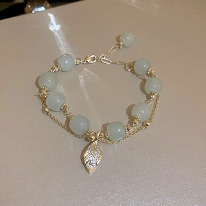 Detail of gold plated leaf charm and light green gemstone beads on double layer bracelet