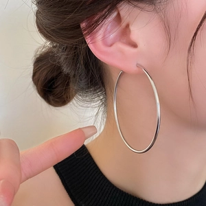 Side view detail of a model wearing large silver-tone minimalist hoop earrings