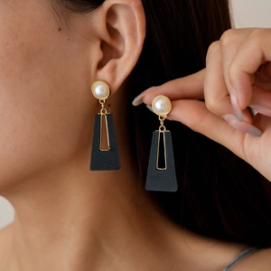 Elegant gold earrings with white pearl and black trapezoid pendant worn by a model