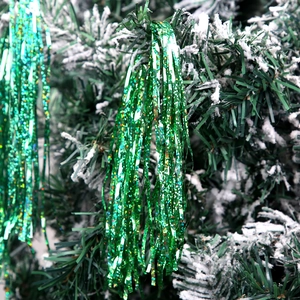 Close-up of sparkling green tinsel fringe decoration hanging on a snowy Christmas tree branch