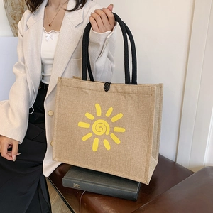 Minimalist linen tote bag with yellow sun print and rope handles on a leather bench