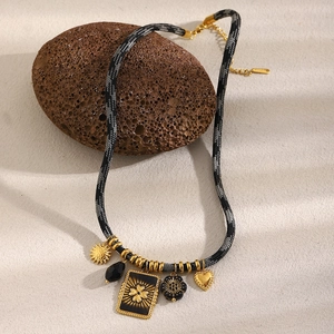 Detailed view of 18K gold-plated floral square pendant and charms on a woven cord necklace