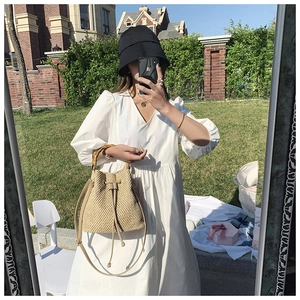 Detail of straw bucket bag with bamboo handle and drawstring closure in outdoor setting
