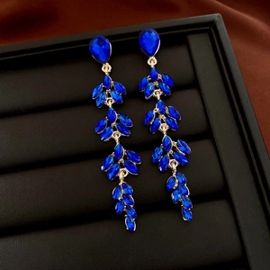 Detail of luxury deep blue crystal tassel earrings with gold metal accents on black texture