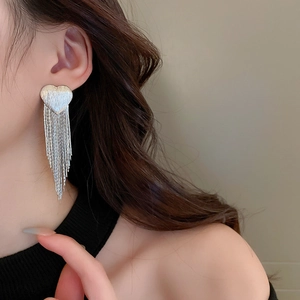 Close-up of long silver tassel heart earrings worn to show elegant drape and movement