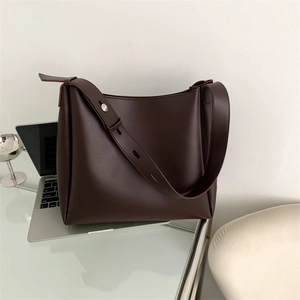 Detail of dark brown leather tote bag showing wide shoulder strap and silver metal buckle