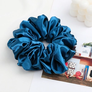 Close-up of deep blue satin scrunchie with glossy pleated texture on white background