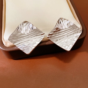 Macro view of textured geometric rhombus earrings in bright silver on leather display