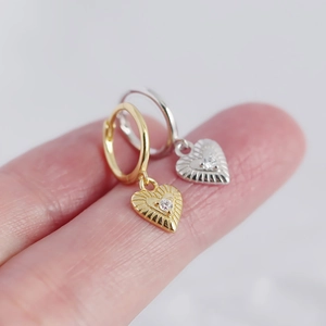 Macro detail of gold and silver heart earrings with zircon on a fingertip model