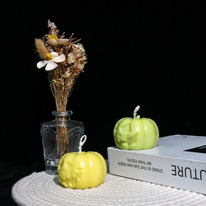 Detail of yellow and green pumpkin candles with carved faces on a white woven mat