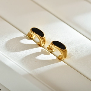 Macro shot of gold C-shaped earrings with black enamel inlay on white leather