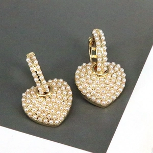 Macro detail of heart-shaped gold earrings with full pave micro pearls on split background