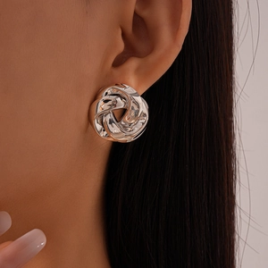 Close-up of silver knot earrings with metallic twisted texture on a model's ear