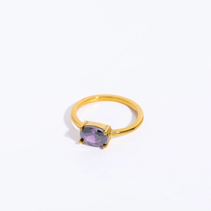 Detailed view of a gold-plated ring with a claw-set oval purple birthstone on white backdrop