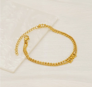 Detail of gold double-layer twist chain bracelet with LOVE pendant on textured background