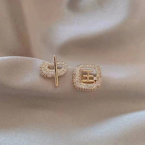 Close-up of asymmetrical gold studs featuring Chinese characters Zhong and Guo with crystals