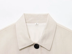 Détail macro de la texture en lin mélangé beige et bouton en résine noire sur la veste