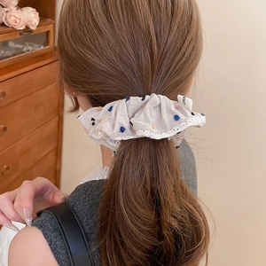 Close-up of beige scrunchie with colorful dots and lace trim worn on a high ponytail