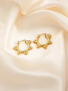 Detailed macro of golden hoop earrings with textured beads on soft silk background