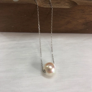 Detail of high-luster white round pearl pendant on s925 silver chain over dark wood