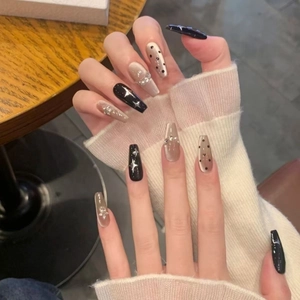Long coffin press-on nails with black stars, dots, and rhinestones on wood background