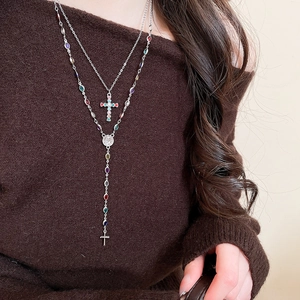 Detail of layered cross necklaces with colorful gemstones on a brown knit sweater