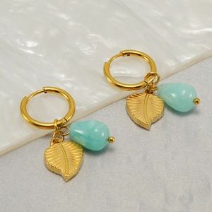 Golden leaf hoop earrings with turquoise teardrop charms on a textured background