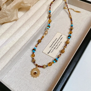 Detail of beaded necklace with gold sun pendant and colorful gems in a velvet jewelry box