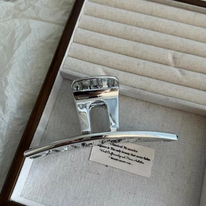 Detail showing high-shine silver metal shark hair claw clip in a beige jewelry box