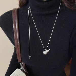 Dettaglio della collana con ciondolo a zucca d'argento e finitura perlata su maglione nero