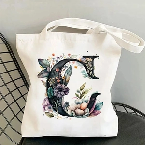 Close-up of a white canvas tote bag featuring a floral alphabet C and black straps