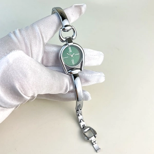 Detail of silver bracelet watch with green dial and roman numerals held in white gloves