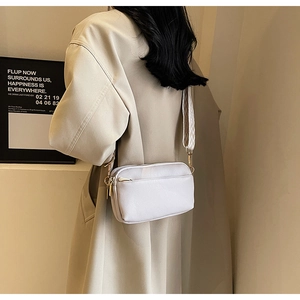 Close-up of minimalist white crossbody bag with patterned wide fabric shoulder strap