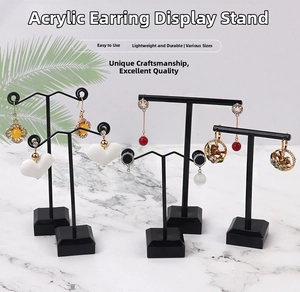 Black acrylic earring stands with T-bar design on white marble surface with palm leaf