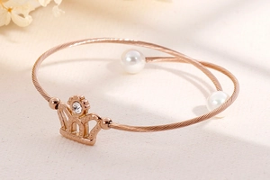 Close-up of rose gold wire bracelet featuring crown motif and white faux pearls