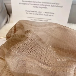 Macro detail of silk wool scarf showing semi-transparent fabric with gold metallic stripes