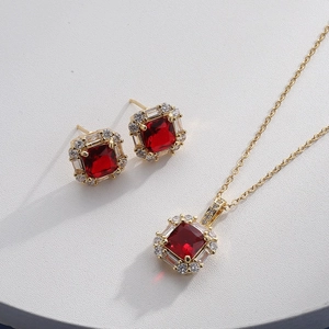 Detail of gold jewelry set with square red gems and clear crystals on white texture