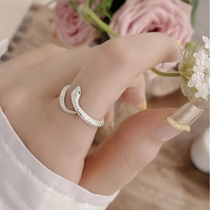Close-up of snake ring with green stone eyes worn on hand with floral background