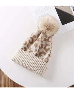 Macro detail of leopard print knit beanie with a fluffy pompom on a white surface
