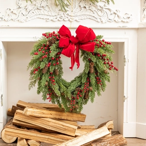 Close-up of heart-shaped Christmas wreath with red berries and bow on a white fireplace