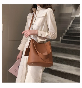 Brown leather bucket bag with top handle and long strap shown with metal bottom studs