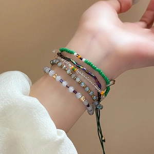 Détail de bracelets bohèmes superposés en perles vertes et mauves sur le poignet
